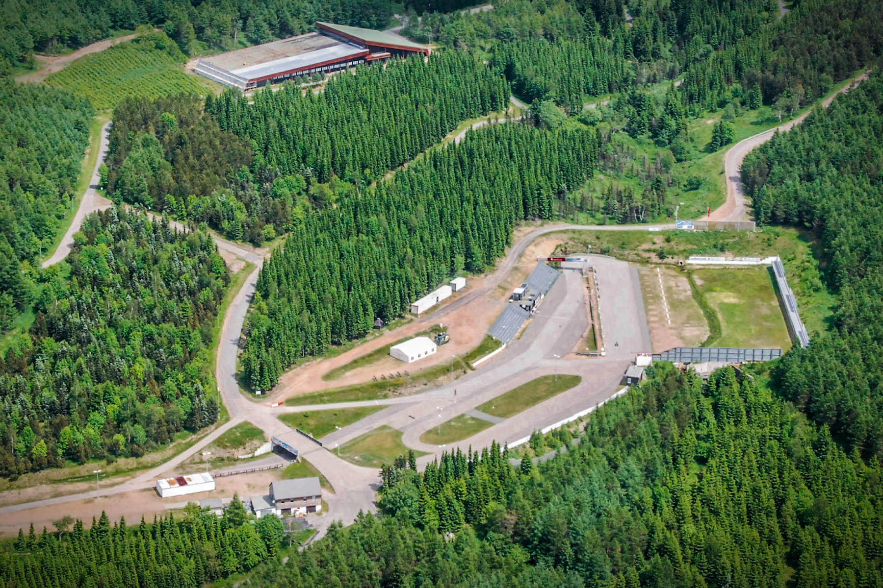 Luftaufnahme einer Biathlonanlage in Altenberg mit Schießständen, Loipen, Gebäuden und Parkplätzen inmitten eines dichten grünen Waldes - ein wahres Zentrum des Sports in Altenberg.